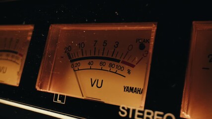 Analog dial indicator of audio signal level amplifier. Vintage arrow moves with sound level. Round classic volume indicator with yellow backlight, VU meters. Close-up of old measuring dB decibels