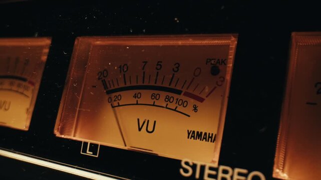 Analog dial indicator of audio signal level amplifier. Vintage arrow moves with sound level. Round classic volume indicator with yellow backlight, VU meters. Close-up of old measuring dB decibels