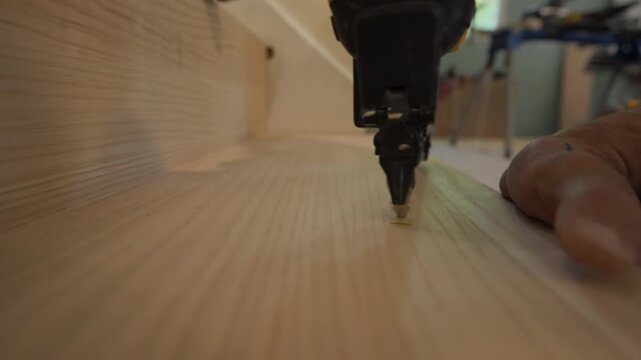 Pneumatic brad nailer securing a wood panel or trim piece into place. Nail gun drives fasteners smoothly, showing craftsmanship and professional home renovation work