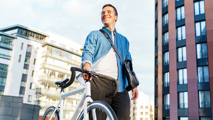 Young man smiles while walking with his bicycle in a modern urban setting