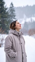 Woman in beige coat standing in snowy field looking upward during calm winter day.
