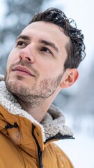 Man outdoors in snowy mountain environment wearing warm jacket with calm thoughtful look.