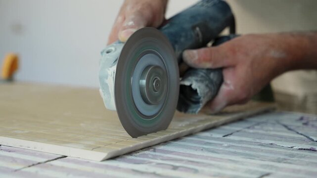 A worker is cutting a ceramic tile with an electric angle grinder. Workshop or renovation site, focusing on craftsmanship, precision, and manual labor.