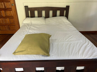 A wooden bed with white sheets and a green cushion in the foreground, at the foot of the bed