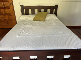 a wooden bed with white sheets and a green cushion at the headboard