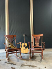 a guitar leaning against a wall, a saxophone on a rocking chair, and an empty rocking chair