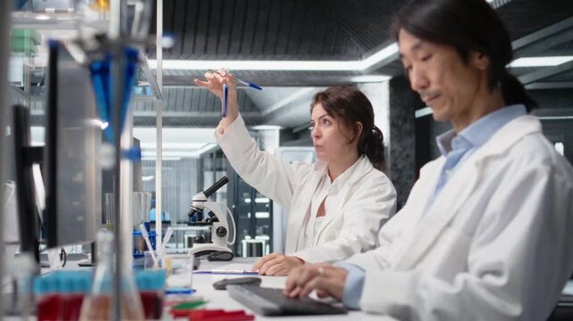 Chemical engineer using laboratory glassware with blue indicator solution in research facility. Chemist looking at cylinder with chemical fluid in lab, analyzing substance properties, camera A