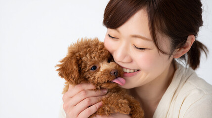 笑顔の女性と舐めて甘えるトイプードルの子犬
