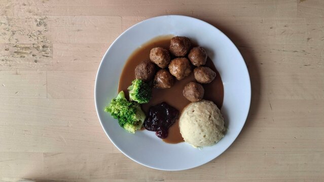 Appetizing plate of IKEA-style Swedish meatballs with gravy, creamy mashed potatoes, and steamed broccoli. Captured in natural light, highlighting the warm and cozy atmosphere of homemade cooking.
