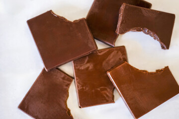 Broken milk chocolate squares scattered on white background