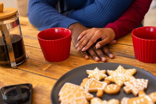 Two hands overlapping on wooden table, with French press beside red mugs and gingerbread cookies - Powered by Adobe