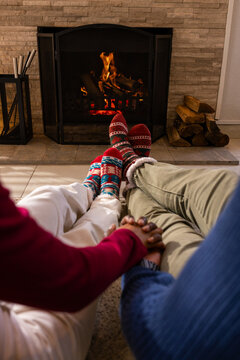 Two pairs of legs and joined hands extending toward stone-faced fireplace with logs in living room