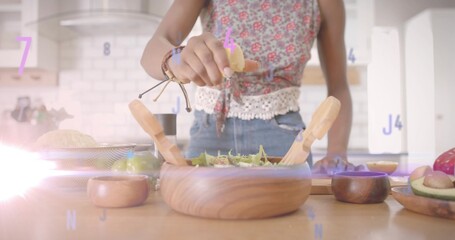Woman in sleeveless top squeezing lemon half over greens at kitchen countertop, with salad bowl