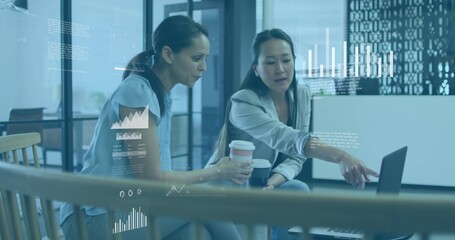 Collaborating mid-adult women pointing at laptop in office lounge, holding takeaway coffee cups