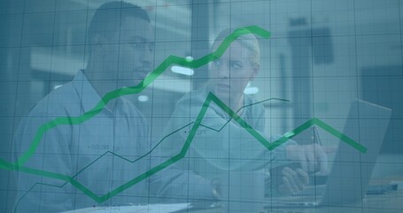 Two office professionals analyzing line charts on laptop in modern office with documents and pen