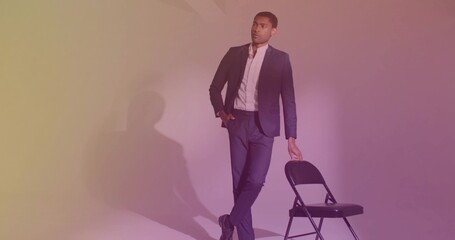 Leaning casually man wearing tailored dark suit and white shirt in studio with black folding chair