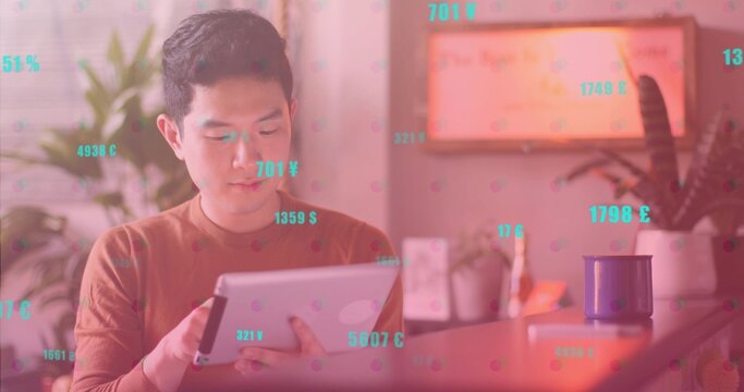 Chinese man wearing brown shirt tapping tablet at desk in home office, floating currency symbols