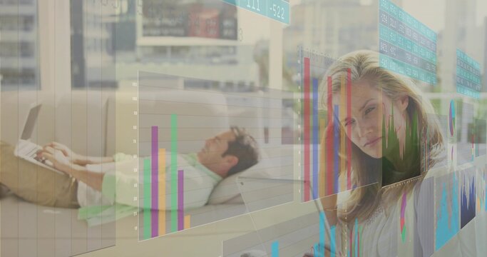 Reclining man working on laptop and woman interacting with holographic charts in modern living room