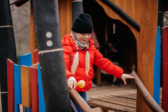 Girl in red jacket and black hat playing on wooden playground.