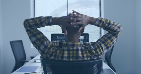 Man in yellow shirt leaning back with hands behind head at office desk, monitor and papers