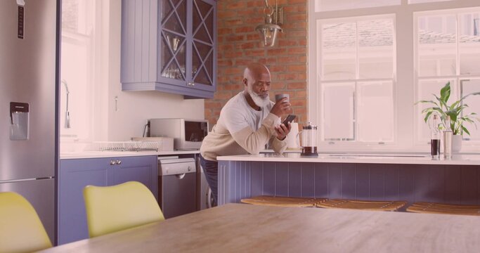 Leaning senior African American man sipping coffee at home kitchen island, with French press mug