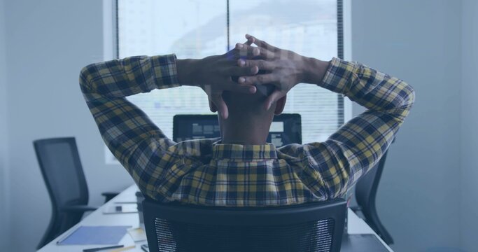 Man in yellow shirt leaning back with hands behind head at office desk, monitor and papers