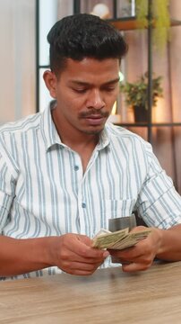 Indian man at home opens wallet counts small bills feels low cash and sighs plans strict budget. Arabian guy at desk checks list of debts sets savings goal cancels extras and writes plan to recover