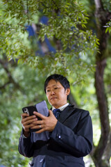 スマートフォンを操作するスーツの男性、夜の公園でスマホを確認するビジネスマン