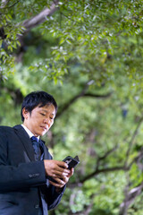 スマートフォンを操作するスーツの男性、夜の公園でスマホを確認するビジネスマン