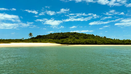 Seascape with an island covered in dense vegetation under a bright blue sky dotted with fluffy...