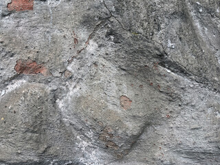 Close-up of a rough stone wall with visible cracks, uneven texture, and patches of exposed brick, showing natural wear and aged surface details.