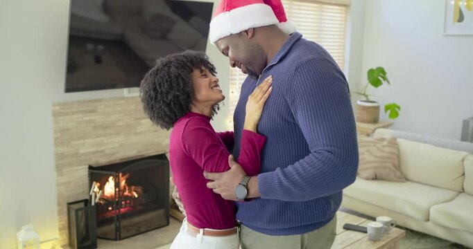 Embracing holiday mood, mid-adult African American couple dancing beside fireplace with Santa hat