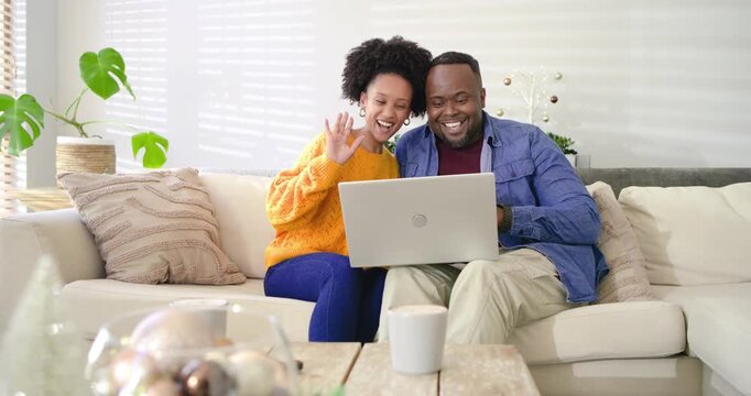 Diverse couple opening laptop on sofa in living room while waving to greet family and laughing - Powered by Adobe