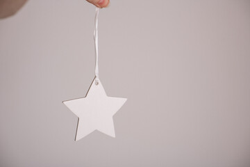 White hanging star on a silver ribbon held by a hand on a light background.