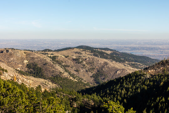 From the mountain heights, the city of Boulder stretches across the valley below, framed by rolling foothills and the vast expanse of the Colorado Rockies.