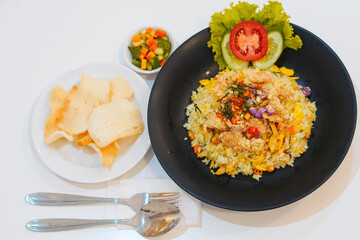 Indonesian Fried Rice with Crackers – Traditional Asian Cuisine. A plate of Indonesian fried rice (nasi goreng), served with crackers, pickles, and fresh vegetables on the side. Traditional Asian cuis