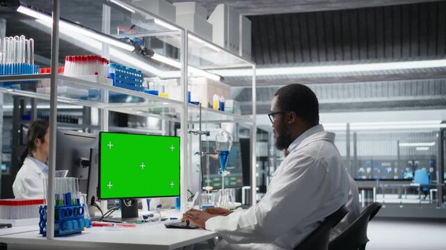 Lab engineer at desk typing on isolated screen PC keyboard, looking at molecular model, doing research tasks. Man using bioengineering program on chroma key computer in medical lab, camera A