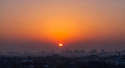 Fototapeta premium Urban city skyline at sunset with vivid orange sky and sun above modern buildings silhouette
