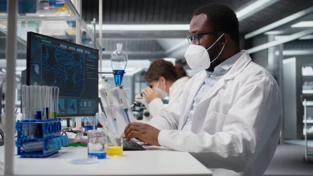 Lab scientist removing protective face mask to scratch beard while using PC. Expert wearing medical mask in contagious workspace studies DNA strand mapping with genomics analysis program, camera A