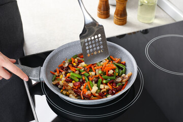 Woman stirring mix of fresh vegetables with slotted spatula in frying pan, closeup