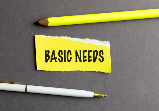 Basic needs words on torn yellow paper with pencil and pen on gray background