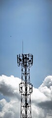 Shadowy telecommunication tower against clouded sky