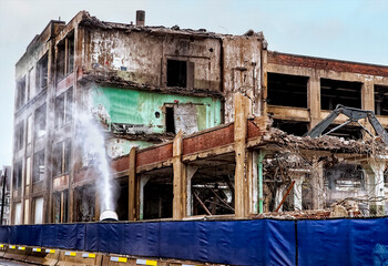 Demolition dust mitigation. A mist of water is being sprayed from a turbine to control dust created by the demolition process. A blue barrier surrounds the area for safety and containment.