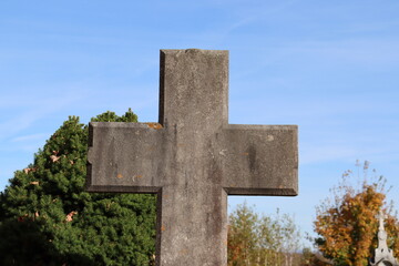 Big old cross in stone in a cemetery in autumn. Religion and life after death.