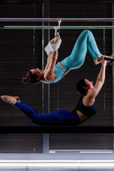 Two women performing an acrobatic routine in a gym while hanging from bars during a training...