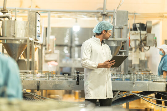 Inspector checking automated machinery in food production facility Focus on quality control safety and workflow efficiency. Worker overseeing food packaging machinery in a modern manufacturing plant.