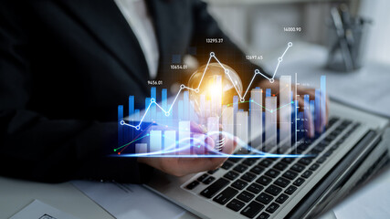 A business professional examines financial data on a laptop, featuring digital charts and graphs...
