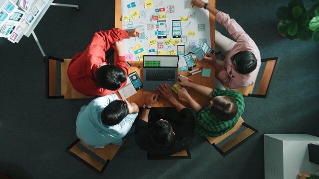 Top view of smart creative project manager using laptop working on Ux Ui design for mobile phone interface while marketing team designing software program by using brainstorming mind map. Convocation. - Powered by Adobe