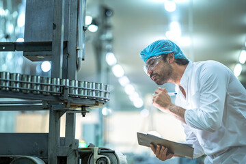 A Quality Assurance (QA) specialist audits a smart factory. He is thoughtfully monitoring an AI driven automated canning line for hygiene and system compliance.