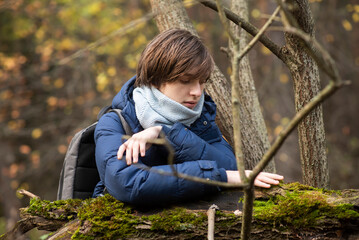 A 13-year-old teenage boy walks in the forest and touches the moss on a tree.